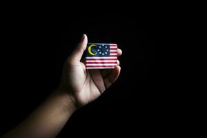 mano Tenere un' attività commerciale carta con il bandiera di il Stati Uniti d'America su nero sfondo, mano Tenere piccolo Malaysia bandiera, ai generato foto