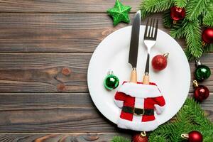 superiore Visualizza di forchetta, coltello e piatto circondato con abete albero e Natale decoratori su di legno sfondo. nuovo anno vigilia e vacanza cena concetto foto