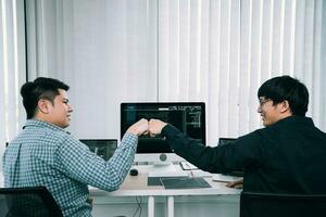 gli sviluppatori di software per dipendenti asiatici celebrano il progetto di successo con un pugno nella stanza dell'ufficio. foto