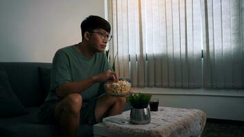 uomo asiatico che guarda una serie di soggiorno mentre mangia un popcorn di notte. foto