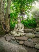 pietra gautama Budda decorativo statua nel un' giardino sotto verde le foglie. all'aperto giardino arredamento concetto. abakan, verticale Visualizza. foto