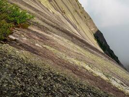 ripido strutturato granito montagna pendenza. pietra struttura. attraversare sezione di rocce. geologica strati. colorato strati di pietre nel sezione di il montare, diverso roccia formazioni e suolo strati. foto