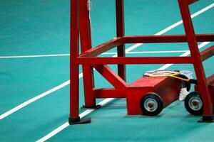 il badminton dell'arbitro sedia è rosso con un' verde badminton Tribunale sfondo foto