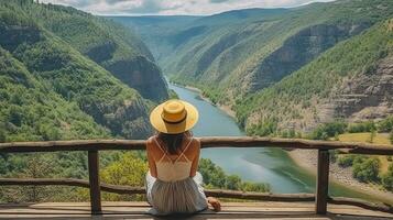 femmina viaggiatore nel cannuccia cappello seduta su di legno pilastro ammirazione mozzafiato scenario di fiume canyon. generativo ai foto