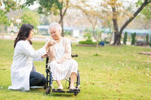 il medico aiuta e si prende cura di una donna anziana asiatica paziente su sedia a rotelle al parco?