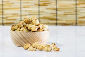 macadamia al forno con salato in ciotola di legno sul tavolo bianco foto