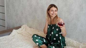 ragazza in pigiama verde a letto con un bicchiere di vino rosso foto