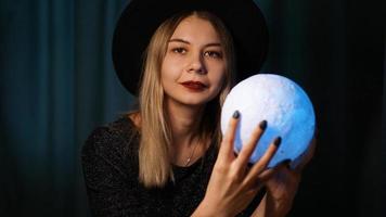 una giovane donna indovino con un cappello tiene in mano una palla magica. foto