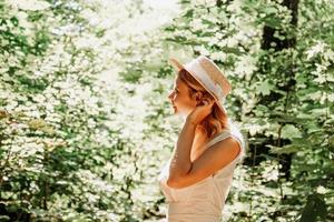 bella giovane donna con cappello di paglia e abito bianco in un parco verde foto