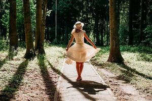 una giovane donna in abito bianco e cappello di paglia cammina nel bosco