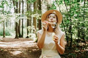 carina donna bionda che soffia bolle di sapone. bellissimo parco verde foto