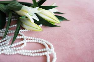 gigli bianchi e una collana di perle su fondo rosa. foto
