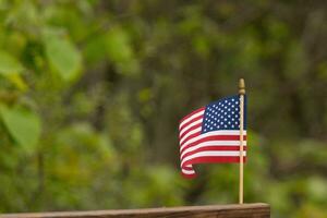 Questo è un Immagine di un' piccolo americano bandiera appuntato per un' di legno trave. Questo patriottico Schermo sembra quaderno colorato con il rosso, bianca, e blu. il simbolo di americano è delicatamente fluente nel il brezza. foto