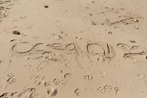 bellissimo Marrone sabbia con scrittura acidato in. il parola oceano può essere visto scritto ione il spiaggia. impronte può essere visto tutti intorno a. foto