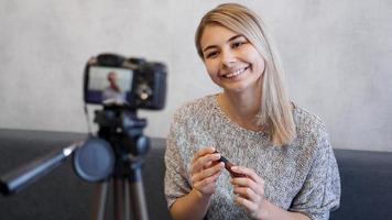 donna vlogger che mostra rossetto. blogger di bellezza in home studio