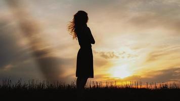 silhouette di una giovane donna in piedi in un campo di erba secca al tramonto? foto