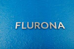 il parola flurona di cui con argento metallo lettere su spiegazzato blu plastica film sfondo foto