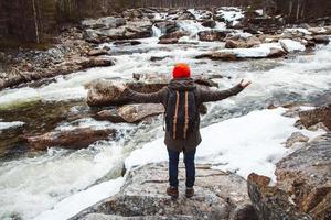 viaggiatore uomo in piedi su una roccia sul fiume di montagna e cascata foto