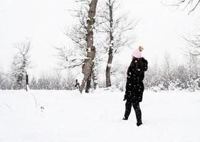 vista posteriore della donna bruna che cammina nel parco innevato in precipitazioni nevose foto