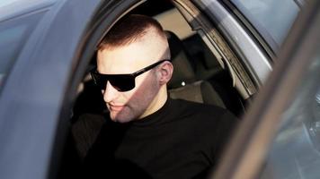 vista laterale del giovane uomo alla moda fiducioso in occhiali da sole nella sua auto foto