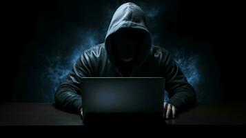 incappucciato scassinatore digitando crimine su buio il computer portatile foto
