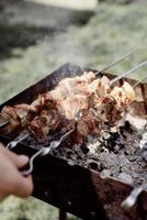 primo piano di spiedini su spiedini, uomo che griglia carne all'aperto foto