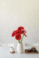 margherite gerbera luminose in vaso bianco sul tavolo da cucina, stile minimal foto