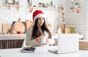 donna con cappello da Babbo Natale che chiacchiera con gli amici usando il suo laptop foto
