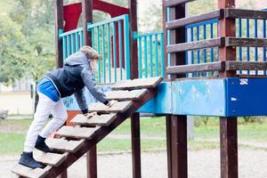 piccolo ragazzo che gioca da solo nel parco giochi a causa della pandemia di coronavirus. foto