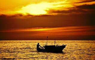 pescatore su il barca al di sopra di drammatico tramonto foto