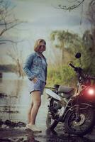 bellissimo donna indossare blu jeans giacca in piedi accanto enduro motociclo contro colorato naturale sfondo foto
