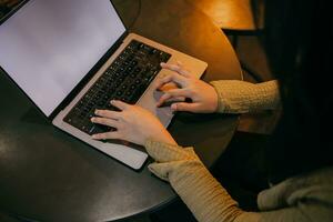 donna utilizzando computer portatile, ricerca il ragnatela, navigazione informazione, avendo un' posto di lavoro a casa con caldo illuminazione intorno a. foto