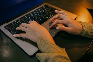 superiore Visualizza di donna di mani digitando su il computer portatile tastiera seduta su sedia e Lavorando in casa con caldo illuminazione. foto