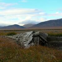 un' di legno edificio distrutto al di sopra di il anni contro un' sfondo di tundra e montagne con nuvole foto