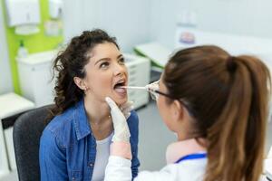 medico con depressore controllo dolorante gola. esperto medico esamina adulto donna per dolorante gola foto