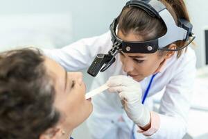 femmina paziente apertura sua bocca per il medico per Guarda nel sua gola. femmina medico l'esame dolorante gola di paziente nel clinica. otorinolaringoiatra esamina dolorante gola di paziente. foto