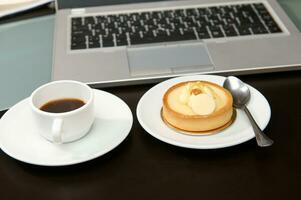 è tempo per prendere un' caffè rompere. un' tazza di appena fermentato caffè espresso e dolce dolce vicino un' il computer portatile. foto