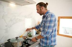 bello italiano giovane adulto uomo in piedi di un' cucina contatore mentre cucinando cena nel minimalista casa cucina foto