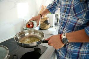 un' frittura padella con vergine oliva olio e baia foglia, un' bottiglia con fresco passata nel il mani di un' capocuoco cucinando cena foto