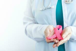 Seno cancro consapevolezza mese. femmina medico nel medico bianca uniforme detiene rosa nastro nel sua mani. Da donna Salute cura foto