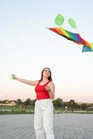 giovane donna che fa volare un aquilone in un parco pubblico al tramonto foto