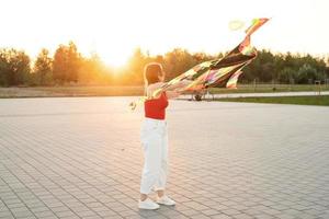 giovane donna che fa volare un aquilone in un parco pubblico al tramonto foto