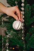 mano femminile che decora l'albero di natale con palline d'argento.