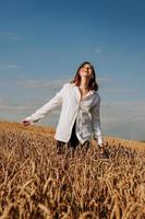 felice giovane donna in una camicia bianca in un campo di grano. giorno soleggiato. foto