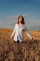 felice giovane donna in una camicia bianca in un campo di grano. giorno soleggiato. foto