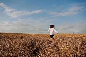 la donna corre in un campo di grano in una giornata estiva. concetto di felicità e gioia foto