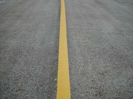 asfalto strada superficie con giallo linea, superficie grunge ruvido di asfalto, buio grigio con giallo linea su il strada e piccolo roccia, struttura sfondo, superiore Visualizza foto