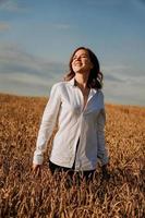 felice giovane donna in una camicia bianca in un campo di grano. giorno soleggiato. foto