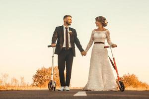 sposi sorridenti in sella a uno scooter lungo la strada al tramonto foto