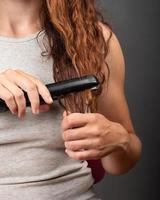 una ragazza con i capelli ricci liscia le ciocche con il ferro, la cura dei capelli. foto